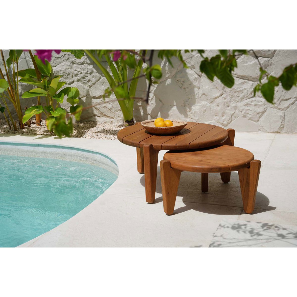 Mise en scène estivale duo table basse en teck posée au bord d'une piscine.