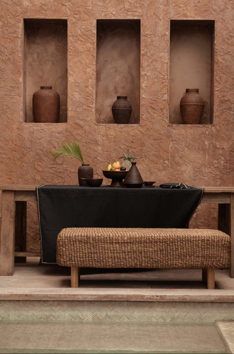 Mise en scène chaleureuse du banc tressé dans un salon aux tons neutres et organiques.