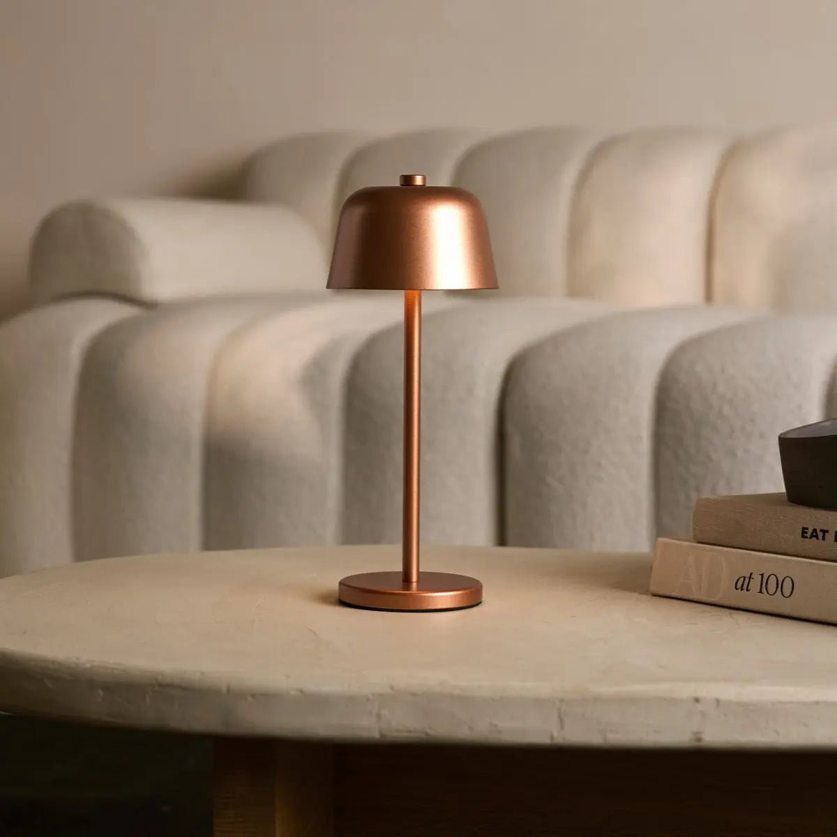 Lampe design cuivre Anton sur table basse devant un canapé blanc confortable.