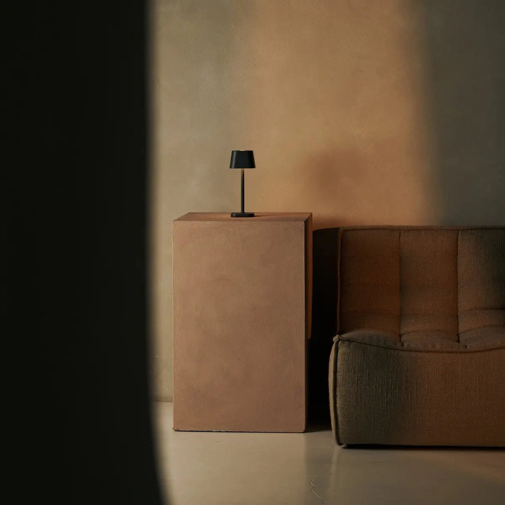 Lampe d'ambiance minimaliste grise dans un coin salon moderne sur socle beige.