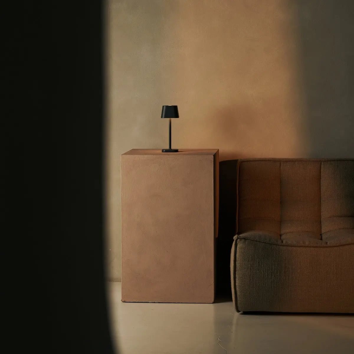 Lampe d'ambiance minimaliste grise dans un coin salon moderne sur socle beige.