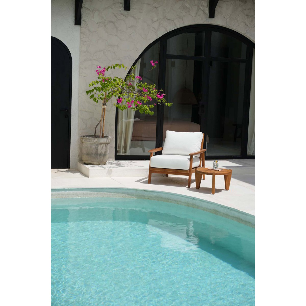 Mise en scène estivale de la table basse en teck posée au bord d'une piscine.
