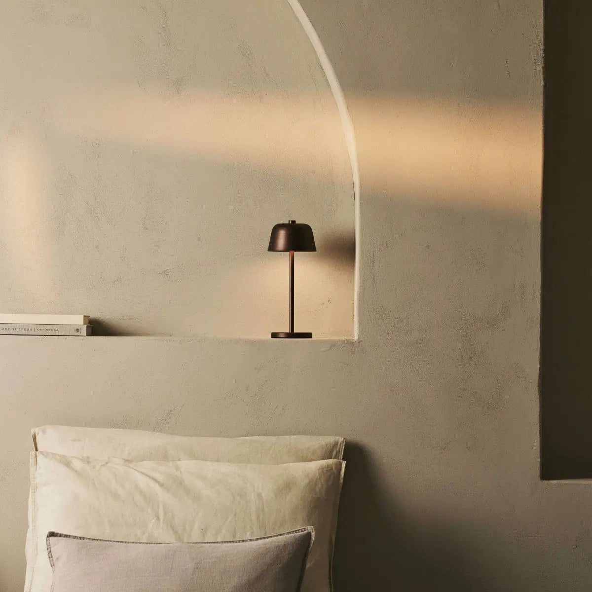 Lampe design bronze Anton posée dans une niche décorative en forme d'arche.