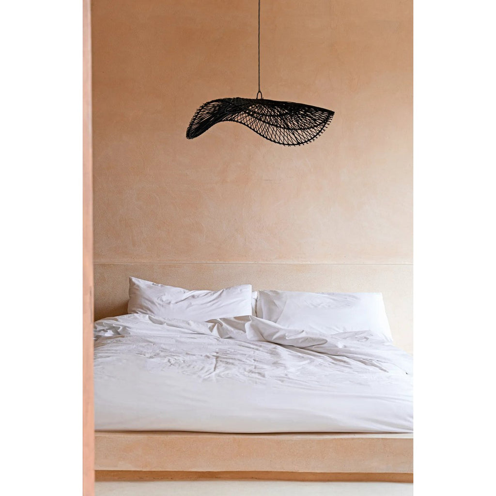 Mise en scène de l'abat-jour en rotin noir au-dessus d'un lit dans une ambiance bohème.