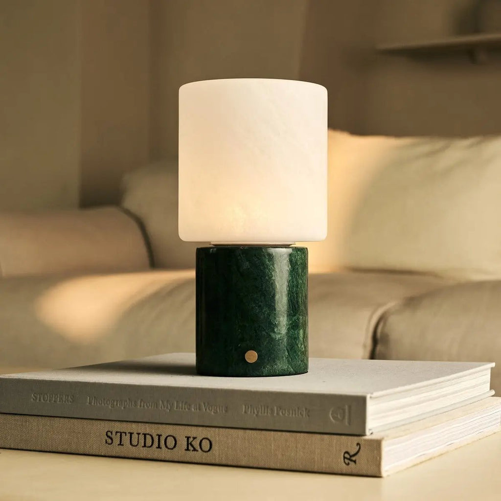 Gros plan sur le socle en marbre Verde Alpi et le bouton tactile doré, posé sur des livres.