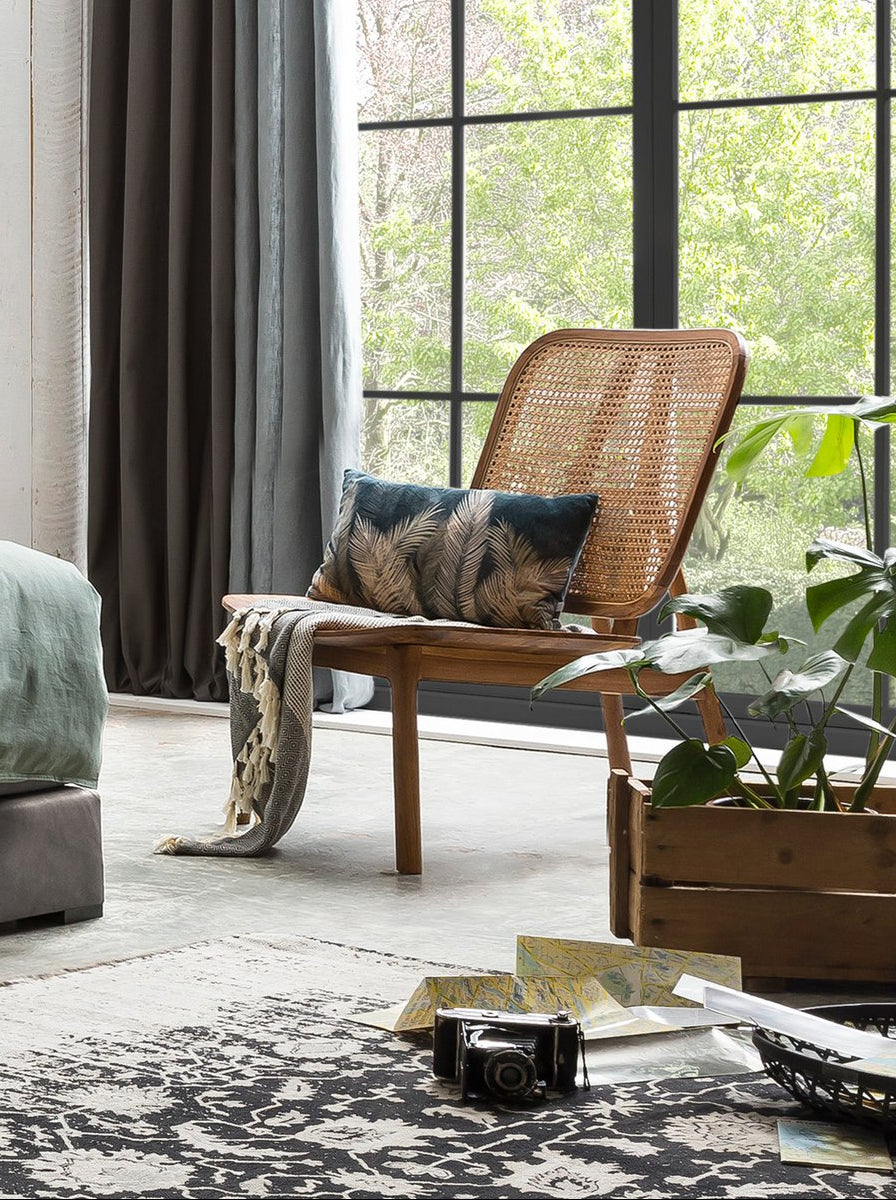 Mise en scène du fauteuil en teck et cannage dans un salon à l'ambiance chaleureuse et lumineuse.