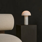 Lampe sculpturale en albâtre blanc diffusant une lumière chaude sur fond noir.