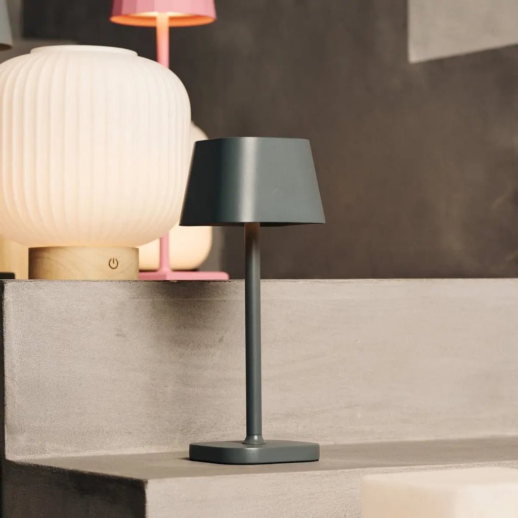 Lampe portable Ava sur un rebord avec ambiance lumineuse chaleureuse en arrière-plan.