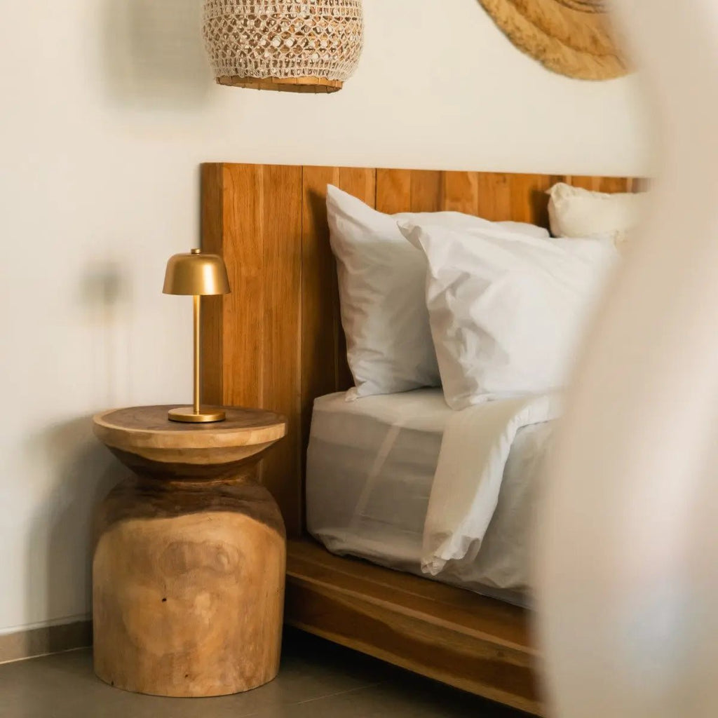 Lampe de chevet tactile dorée posée sur une table de nuit en bois près d'un lit.