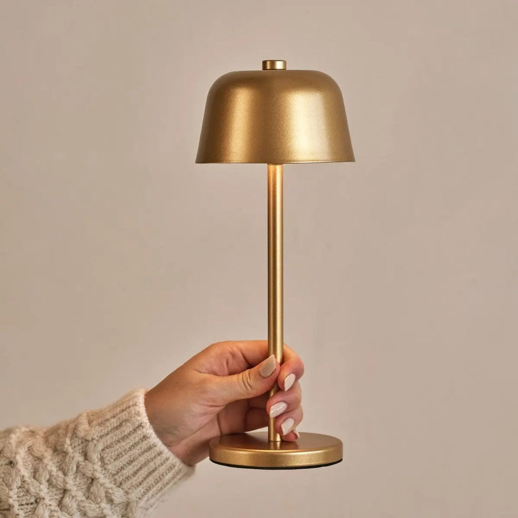 Main tenant la lampe nomade dorée pour montrer sa portabilité et sa taille compacte.