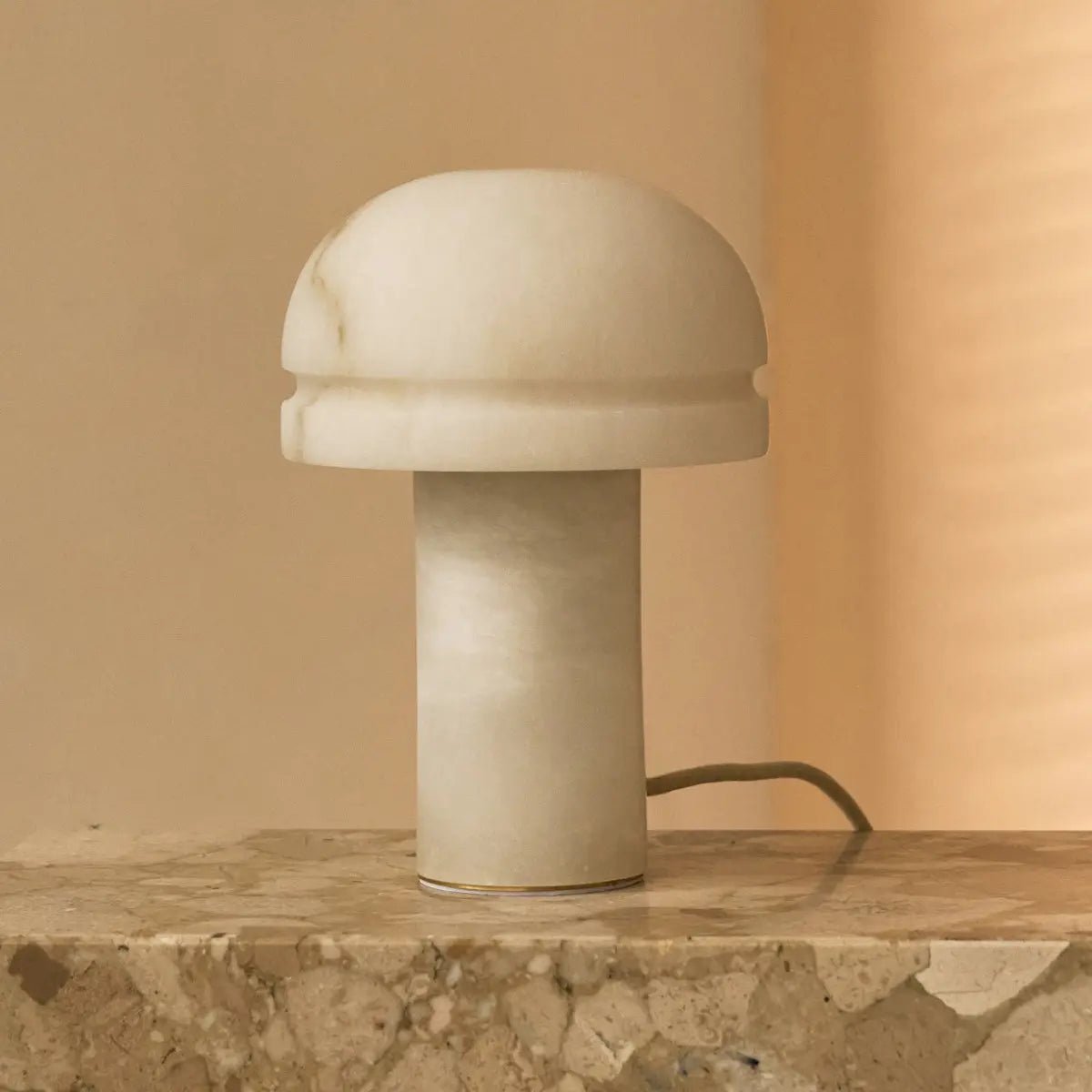 Lampe design champignon en albâtre Leonardo posée sur une table en pierre naturelle.