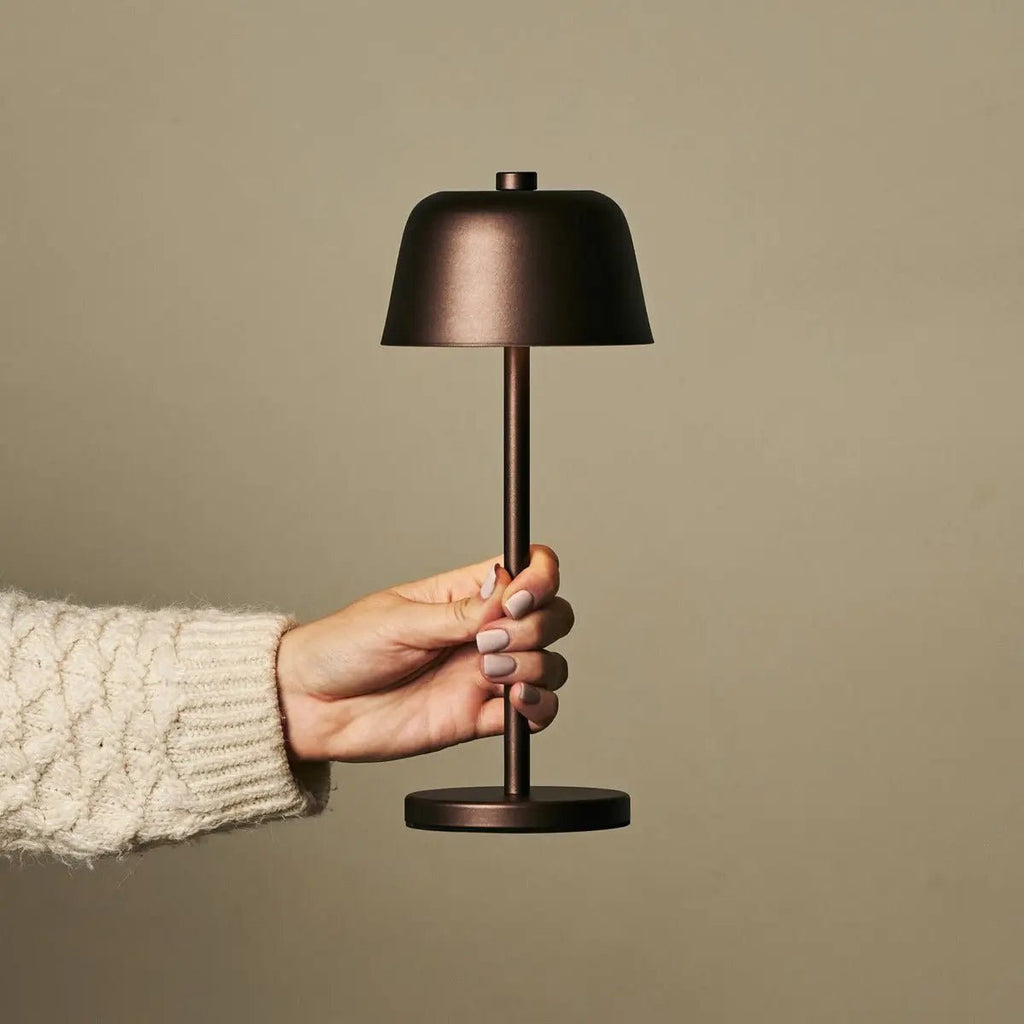 Main tenant la lampe nomade Anton marron pour montrer sa facilité de transport.