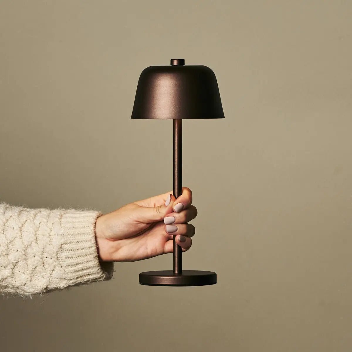 Main tenant la lampe nomade Anton marron pour montrer sa facilité de transport.