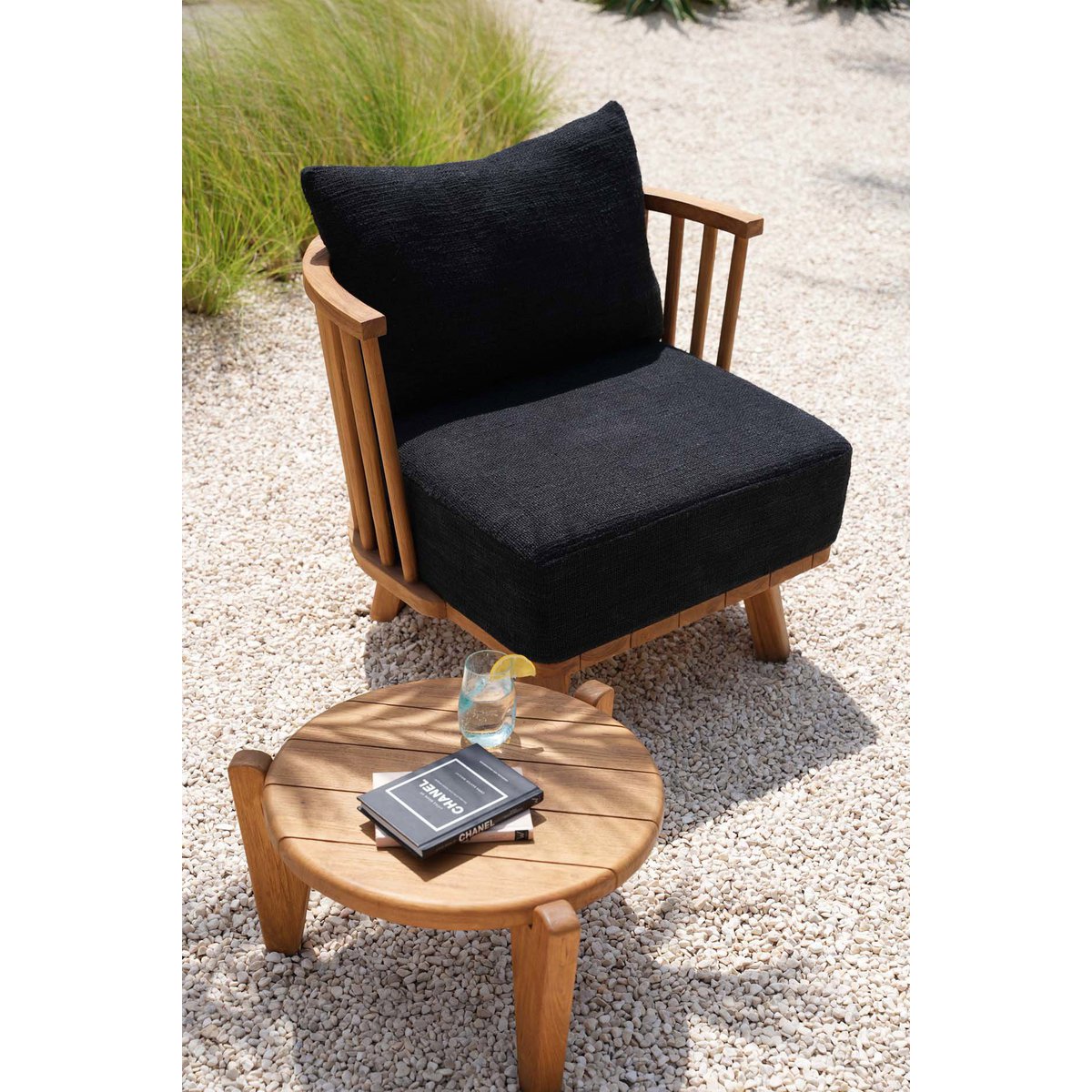 Mise en scène estivale de la table basse en teck posée avec un fauteuil noir en teck.