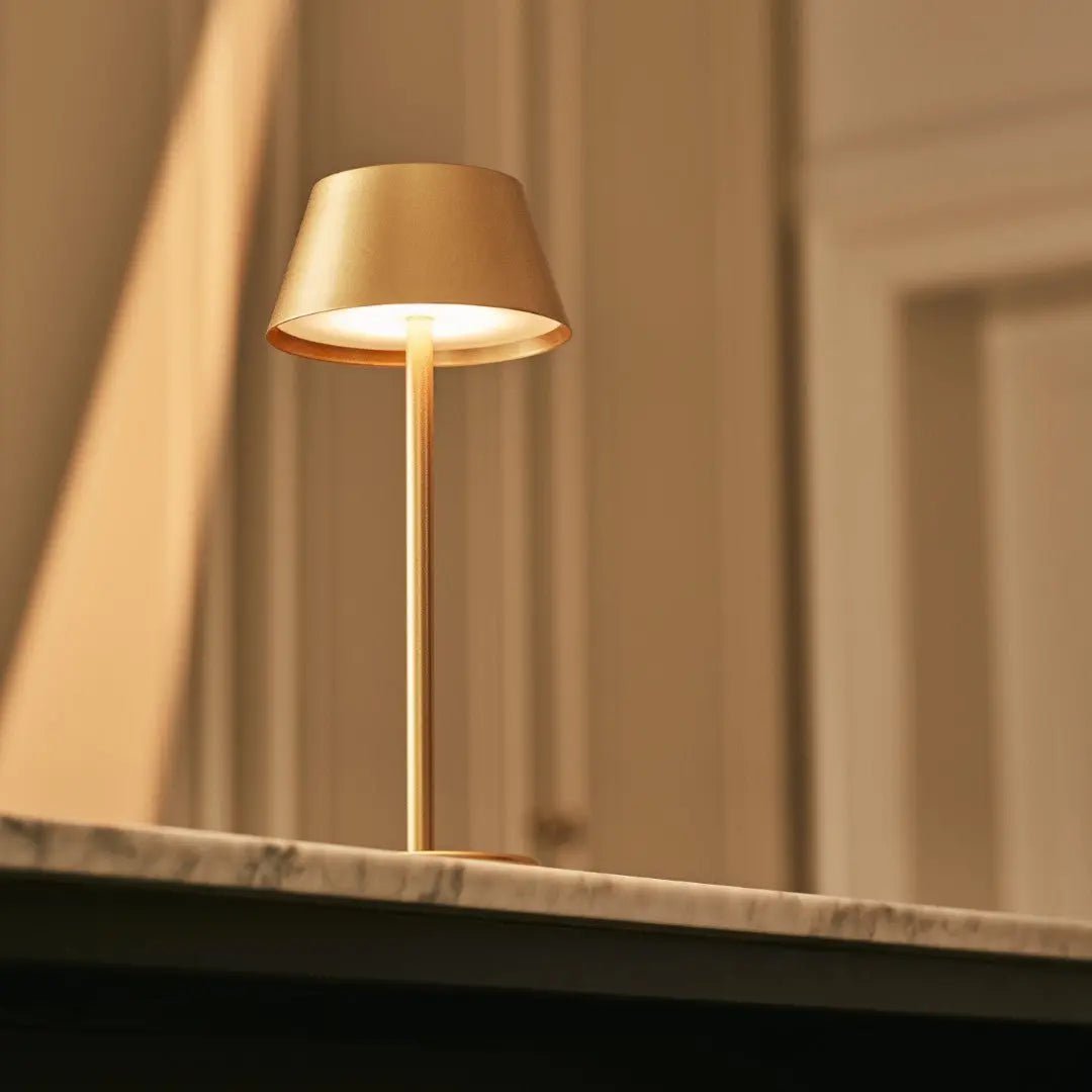 Lampe sans fil or posée sur un comptoir sombre pour une ambiance feutrée.
