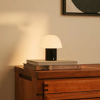 Lampe de table rechargeable Yannick posée sur des livres, posé sur une commode.