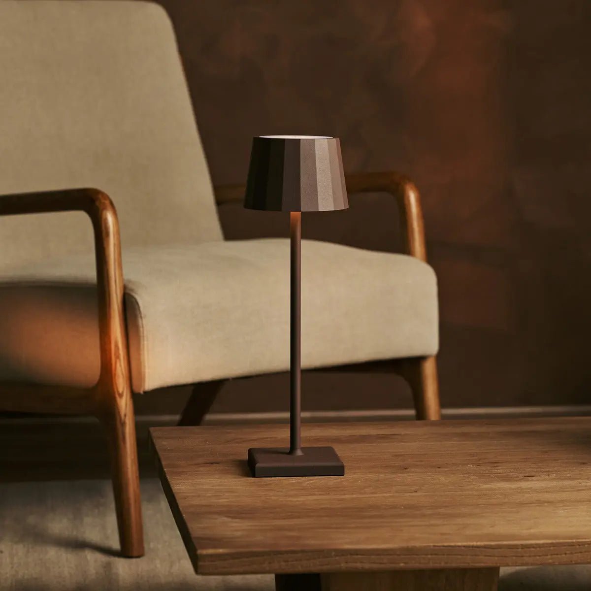 Lampe sans fil marron moka Tavellio posée sur une table d'appoint à côté d'un fauteuil rétro.