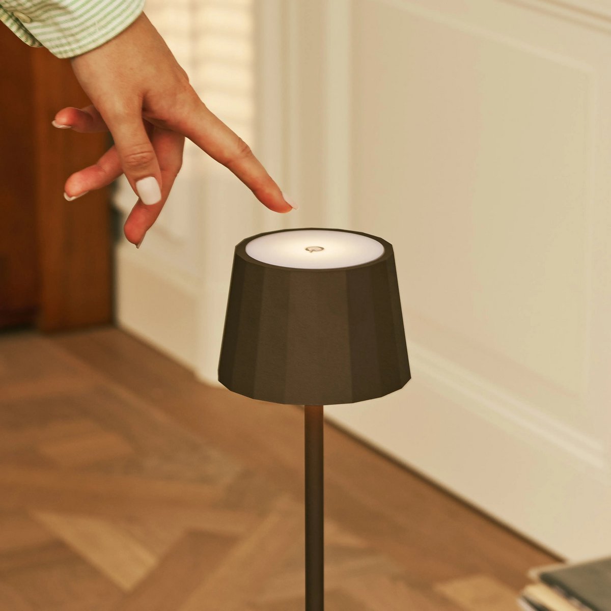 Main utilisant le variateur tactile sur le dessus de l'abat-jour de la lampe nomade Wouter moka.