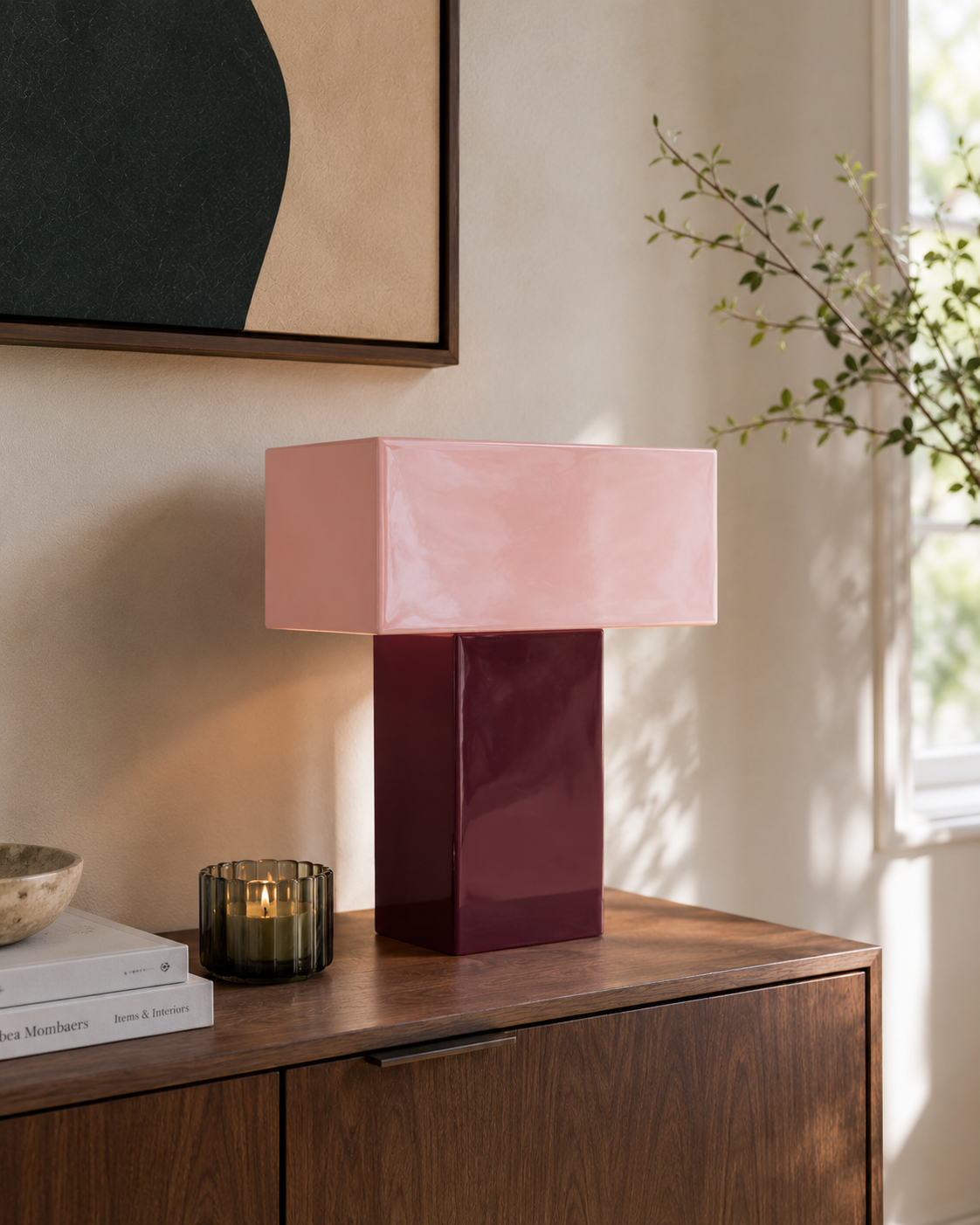 Lampe de table Grato Recto bordeaux et rose poudré posée sur console en noyer avec bougie fumée et branche végétale tableau abstrait noir et beige ambiance salon contemporain