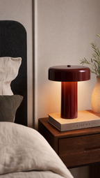 Lampe de table rouge bordeaux allumée posée sur livre Kinfolk table de chevet en bois ambiance chambre cosy éclairage chaud style contemporain