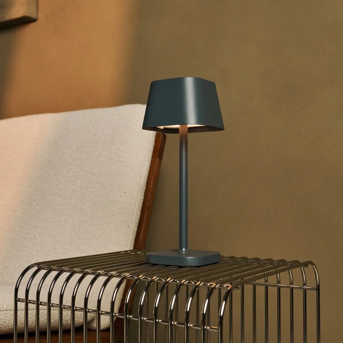 Lampe nomade Ava Stone Grey sur une table d'appoint en métal filaire noir.