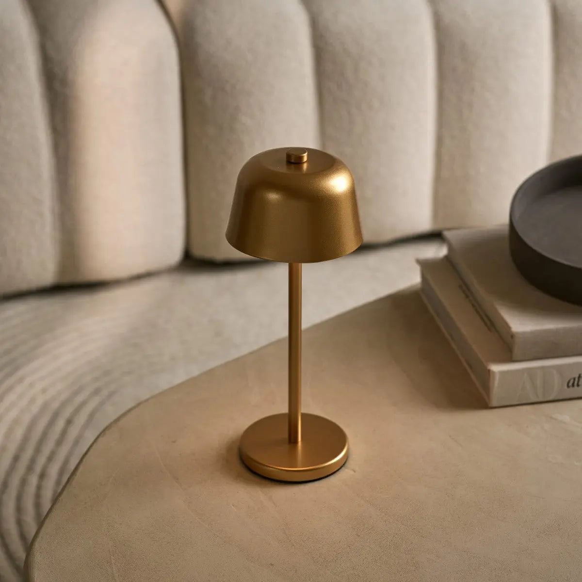 Lampe de chevet tactile dorée posée sur une table de nuit en bois près d'un lit.
