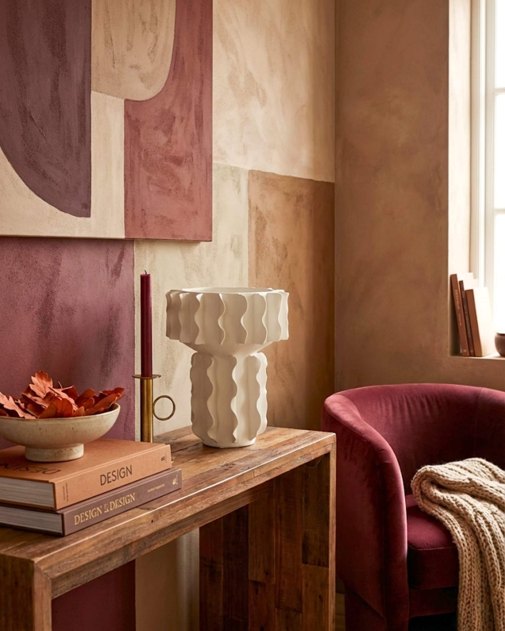 Décoration salon élégant : grand vase blanc design Hélios mis en scène sur un meuble en bois, à côté d'un fauteuil en velours bordeaux et d'un tableau abstrait.