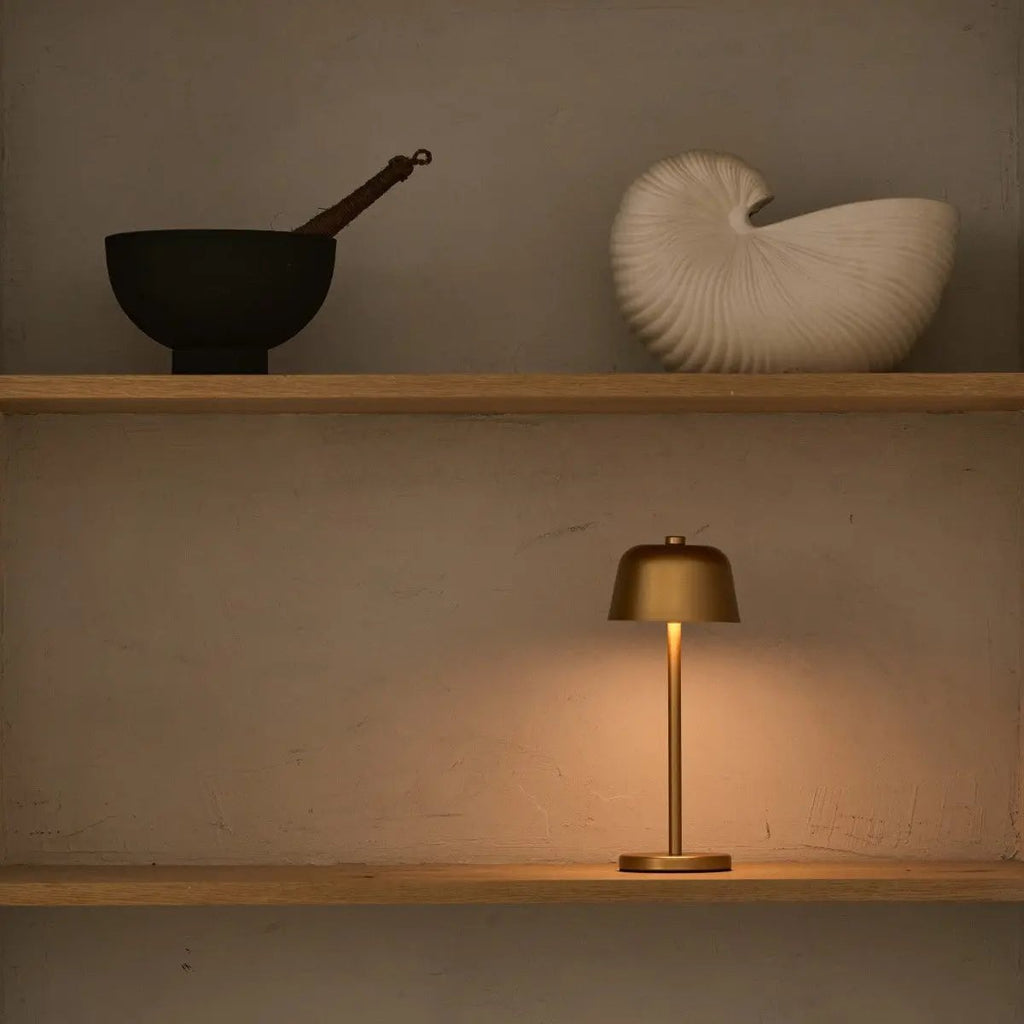 Lampe design minimaliste dorée posée sur une étagère comme objet de décoration.