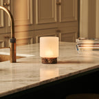 Lampe de table sans fil Cuyp posée sur un plan de travail, base en marbre brun Emperador et abat-jour en verre illuminé.