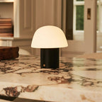 Lampe de table sans fil en bois noir et verre allumée sur un comptoir de cuisine.