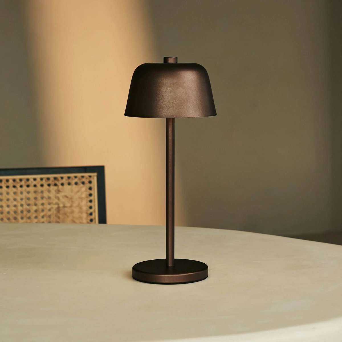 Lampe sans fil couleur espresso Anton posée sur une table ronde blanche minimaliste.