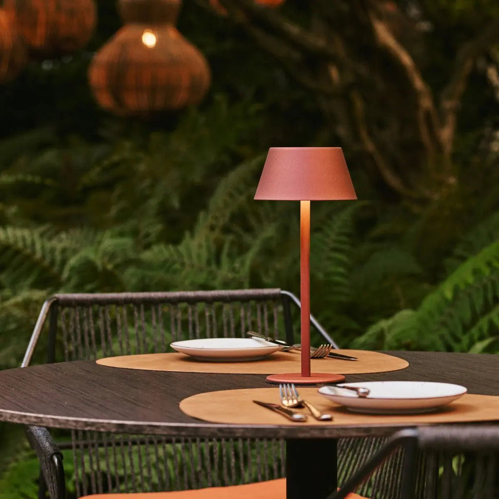 Lampe nomade posée sur une table extérieure avec végétation en fond.