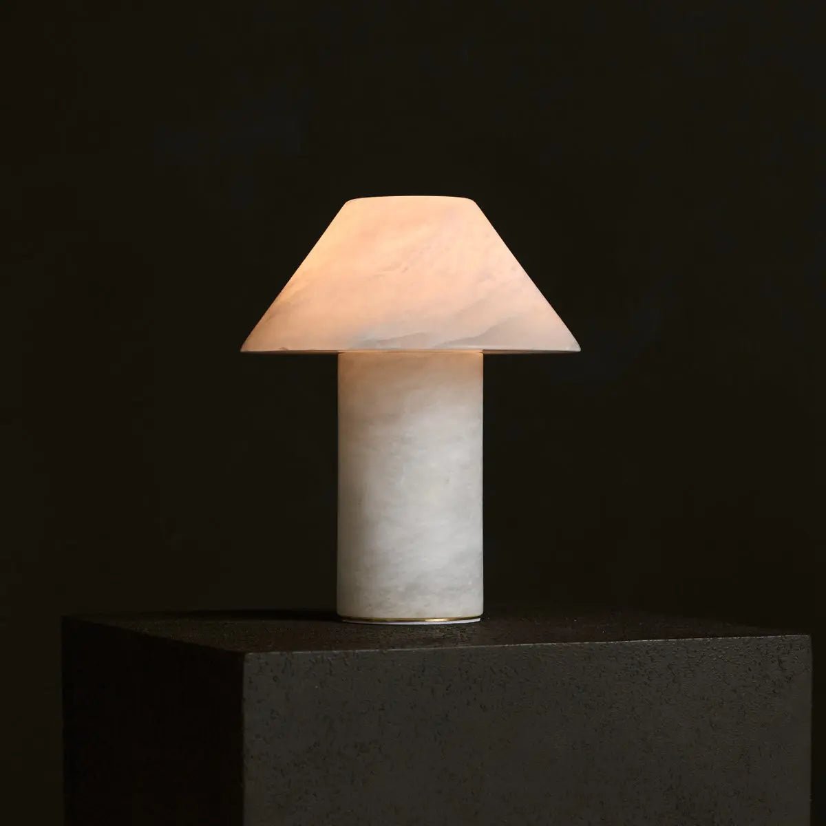 Lampe design en albâtre diffusant une lumière chaude sur fond sombre.