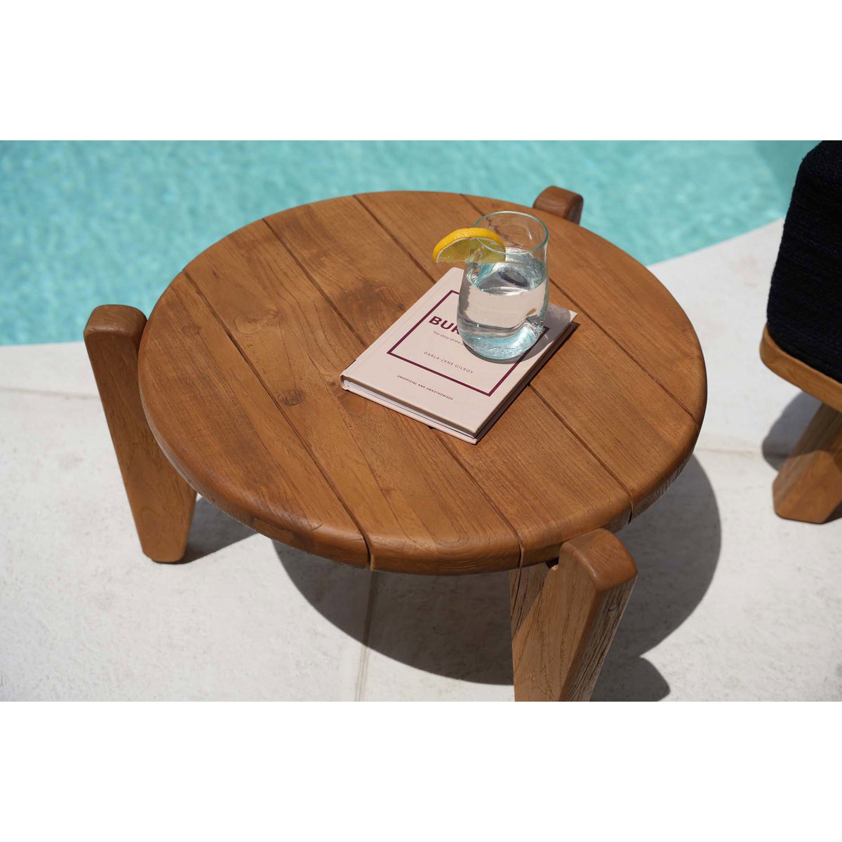Mise en scène estivale de la table basse en teck posée au bord d'une piscine.