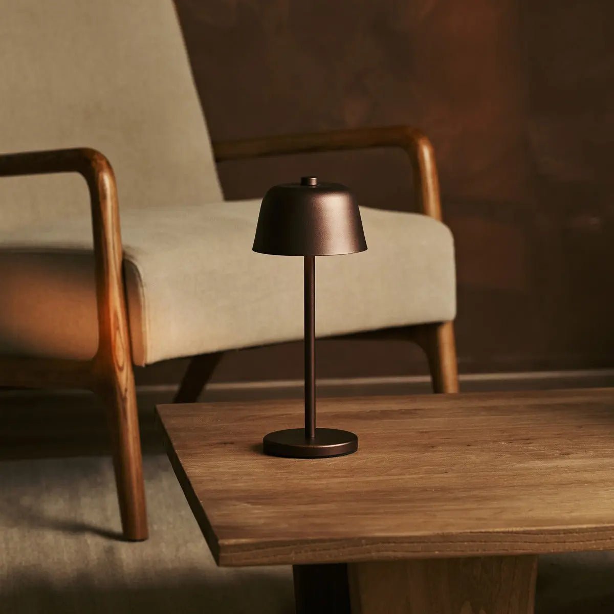 Lampe de table rechargeable Anton Espresso marron posée sur une table basse en bois foncé.