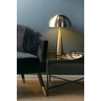 Lampe de table argentée allumée posée sur un meuble en bois devant un mur bleu