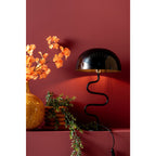 Lampe à poser noire allumée dans une décoration colorée, diffusant une lumière chaude et tamisée sous son abat-jour dôme.