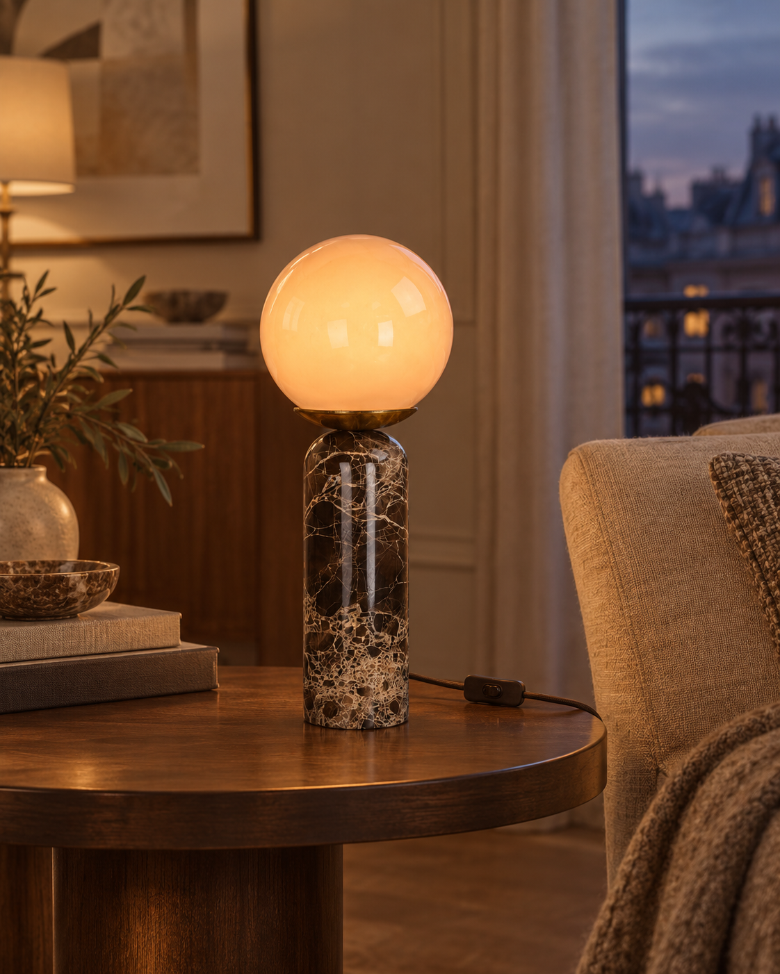 Lampe LAZIO Sphère allumée sur une table près d’un fauteuil, dans un salon à l’ambiance chaleureuse.