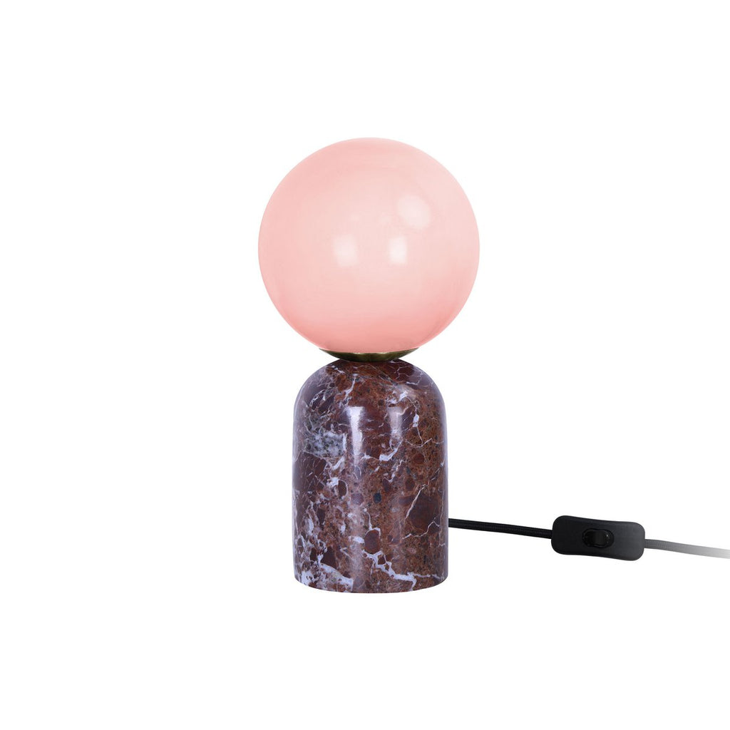 Lampe LAZIO Sphère Petite allumée sur fond blanc, globe rosé sur socle en marbre veiné, avec interrupteur sur le câble noir.
