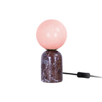 Lampe LAZIO Sphère Petite allumée sur fond blanc, globe rosé sur socle en marbre veiné, avec interrupteur sur le câble noir.