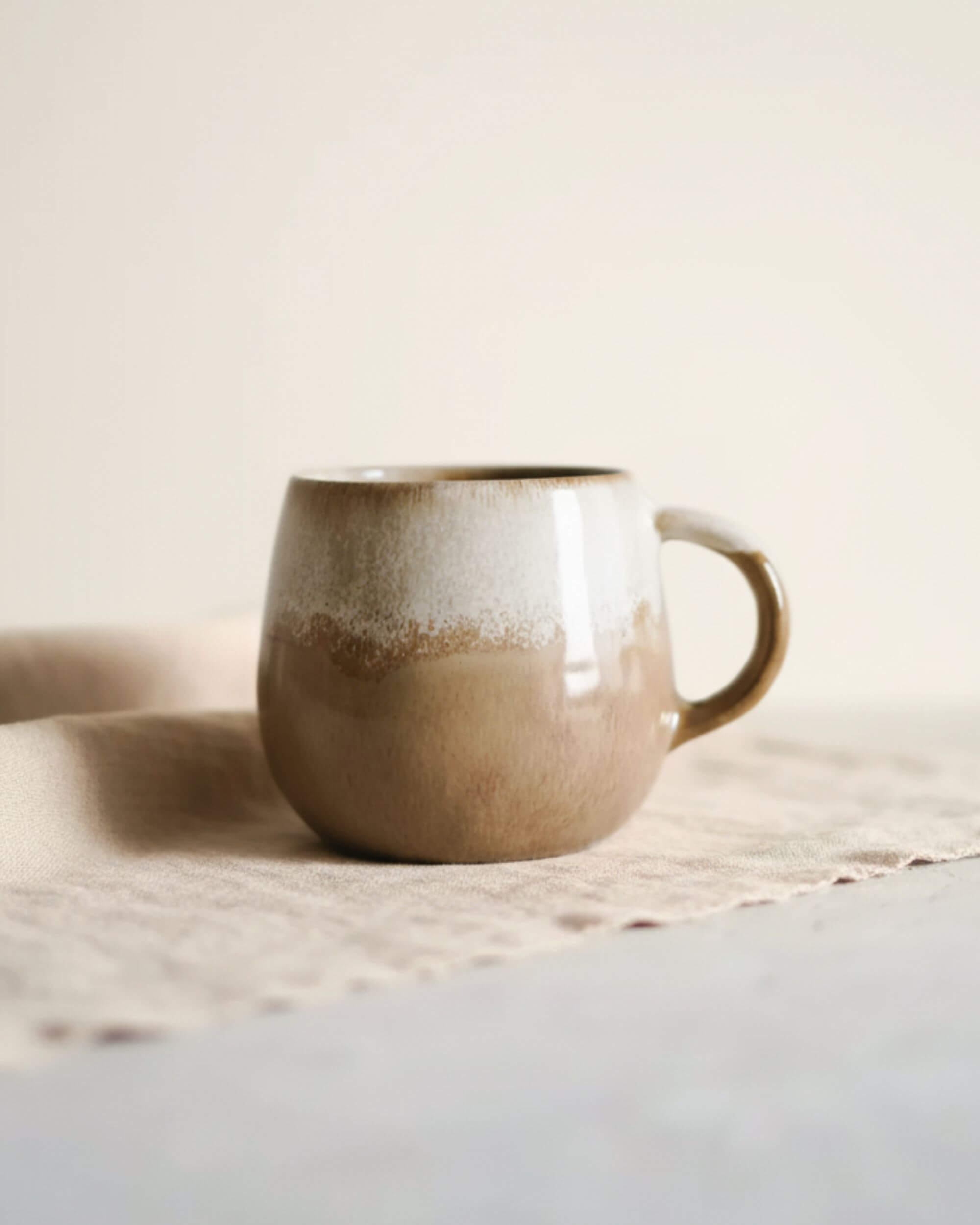 Main tenant le mug DUNES en céramique beige et caramel, fait main