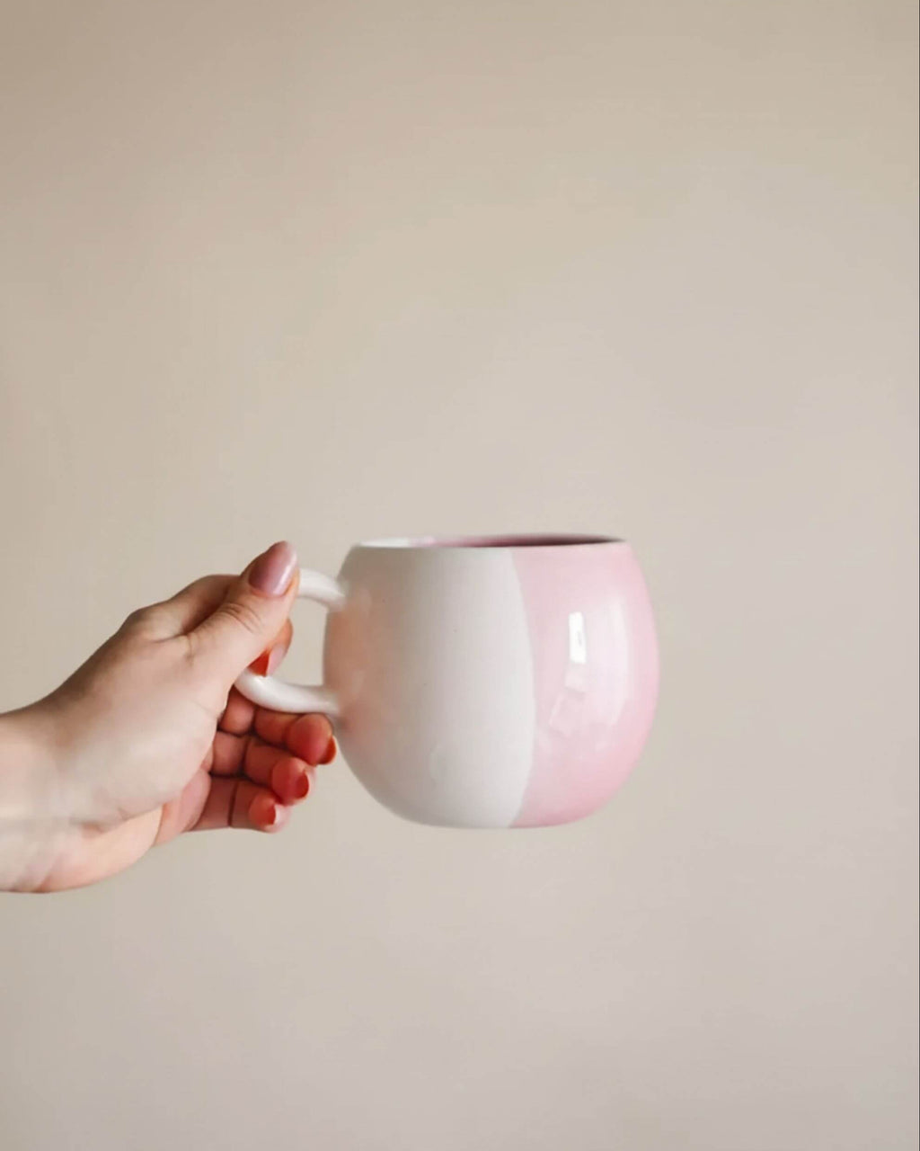 Main tenant le mug artisanal SOUPIR rose et blanc, design rond et fait main au Portugal.