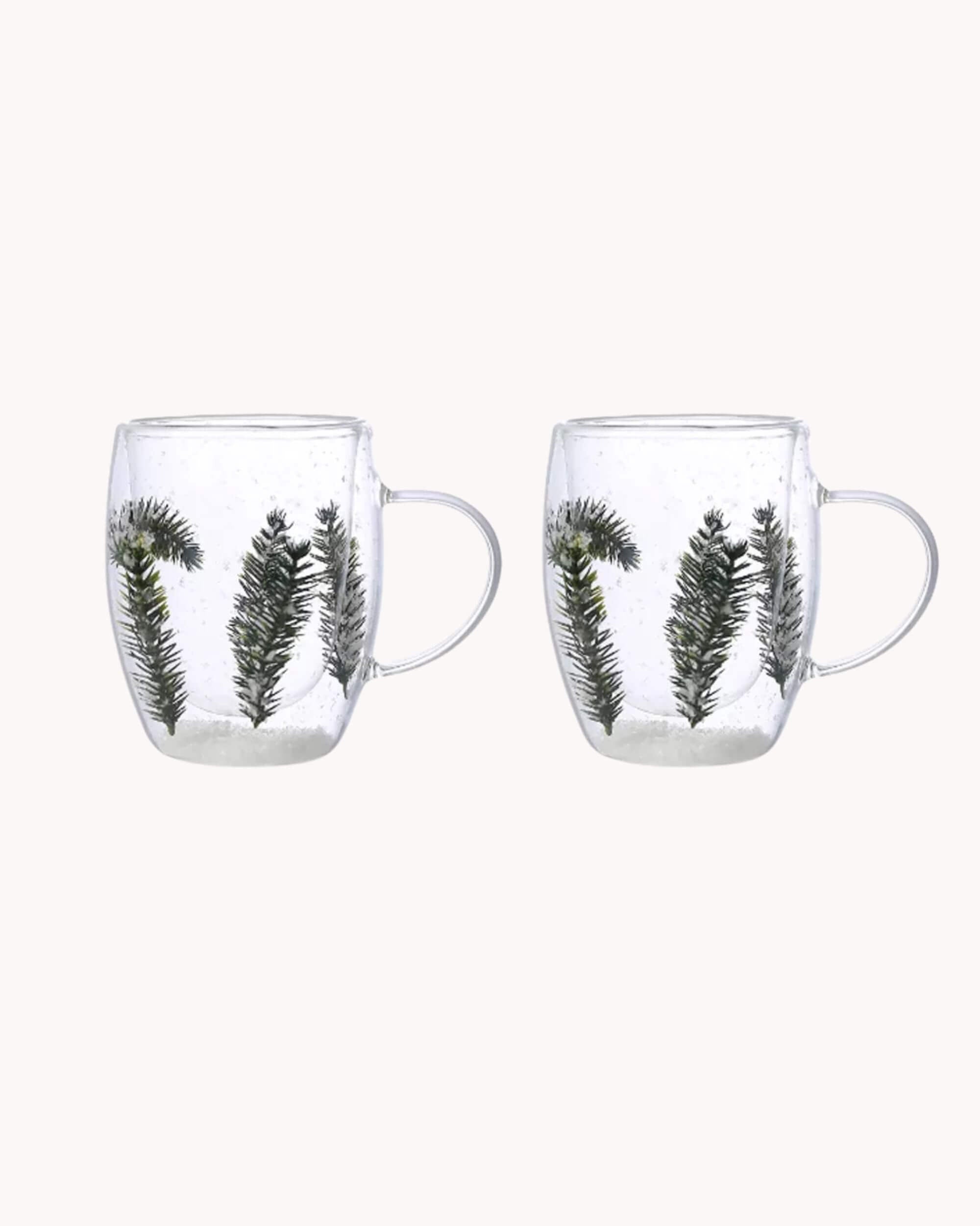 Lot de deux mugs en verre double paroi avec sapins et neige, vue packshot sur fond blanc.
