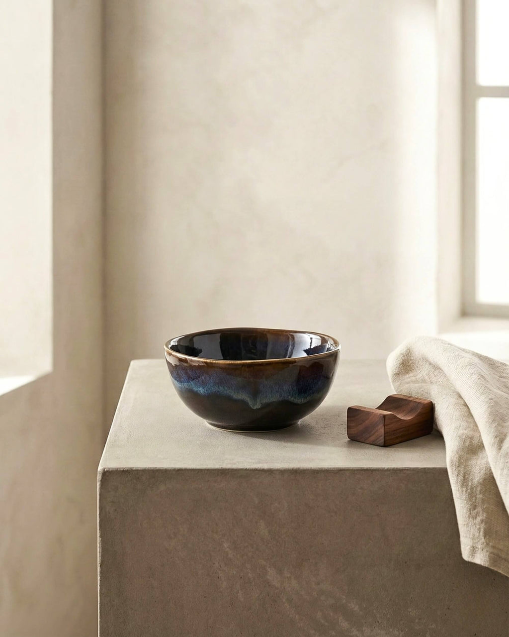 Petit bol apéritif Grawa en céramique émaillée bleu nuit et marron, posé sur un socle en pierre brute. Décoration minérale épurée.