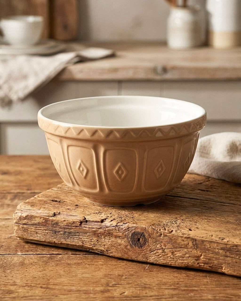 Saladier Livia en céramique beige avec motifs en relief posé sur une planche en bois rustique. Ambiance cuisine chaleureuse.