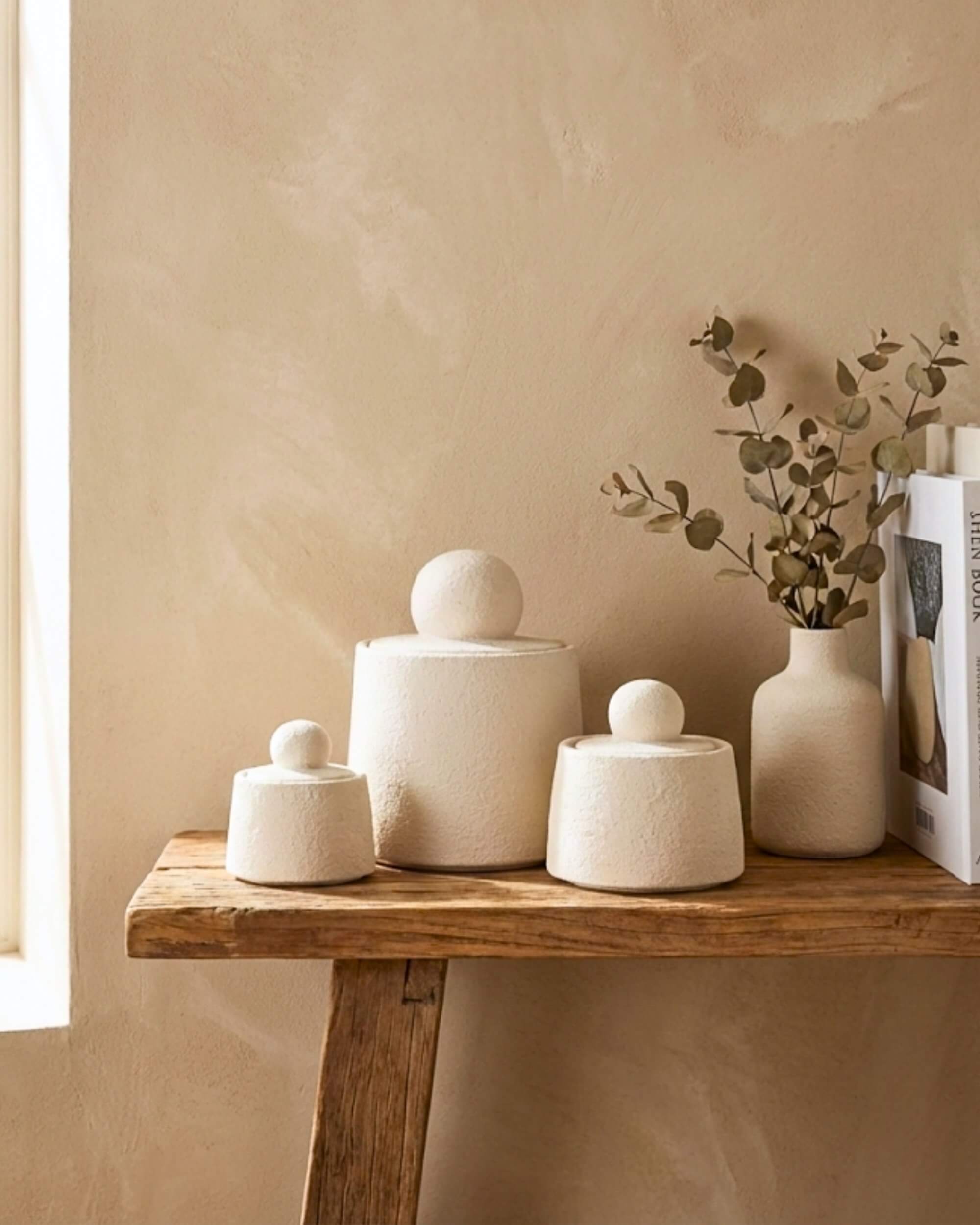 Set de 3 boîtes Olympe en ciment beige texturé posées sur une console en bois brut avec un vase d'eucalyptus, ambiance wabi-sabi naturelle.