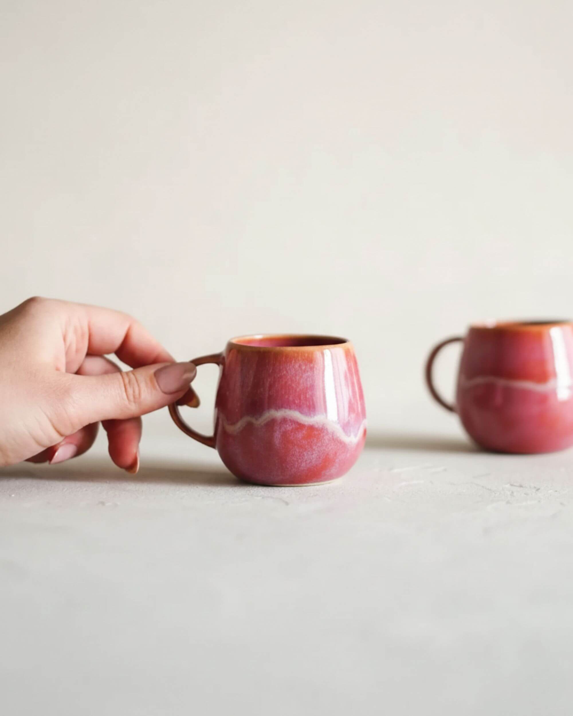 Main tenant la tasse artisanale GUIMAUVE rose et orangé, émail brillant et fait main au Portugal.