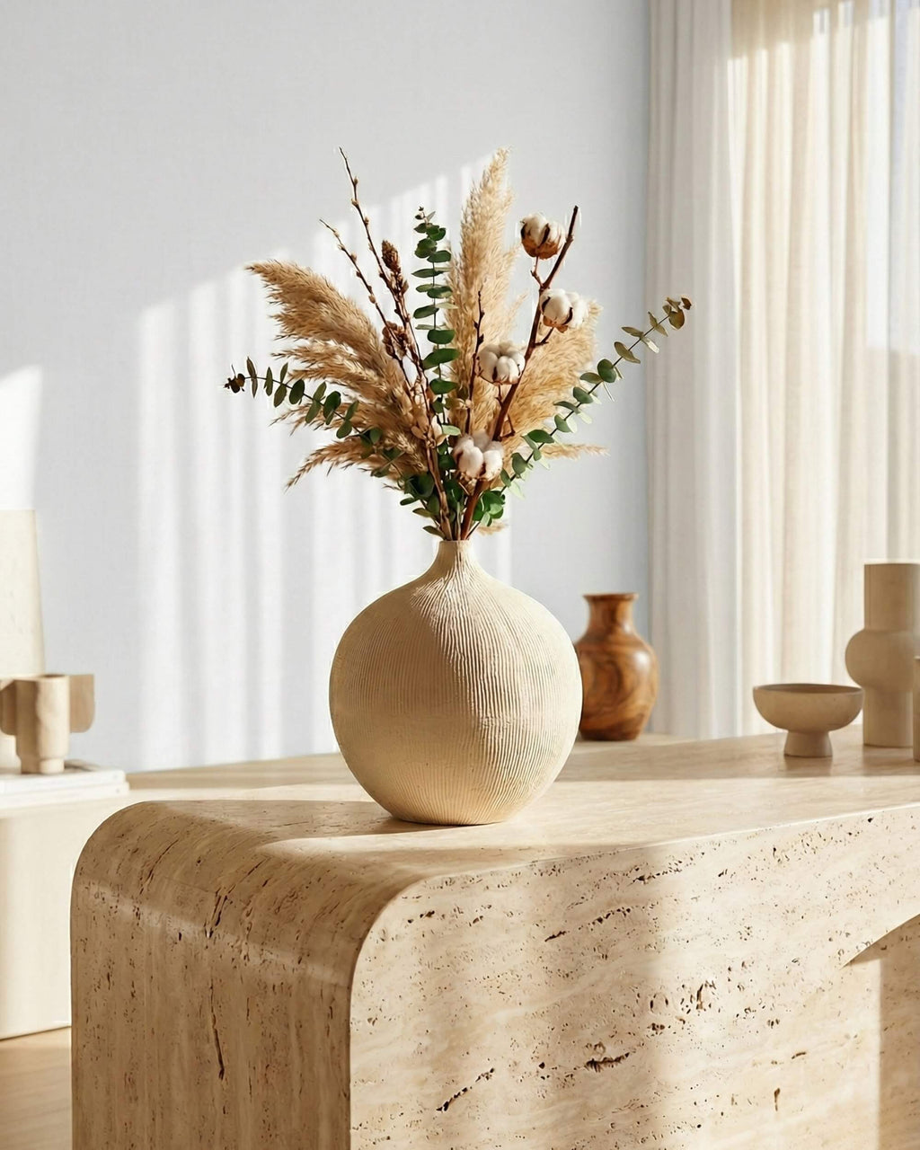 Vase boule Arena en céramique beige texturée garni de fleurs séchées, posé sur une console en travertin. Décoration scandinave lumineuse.