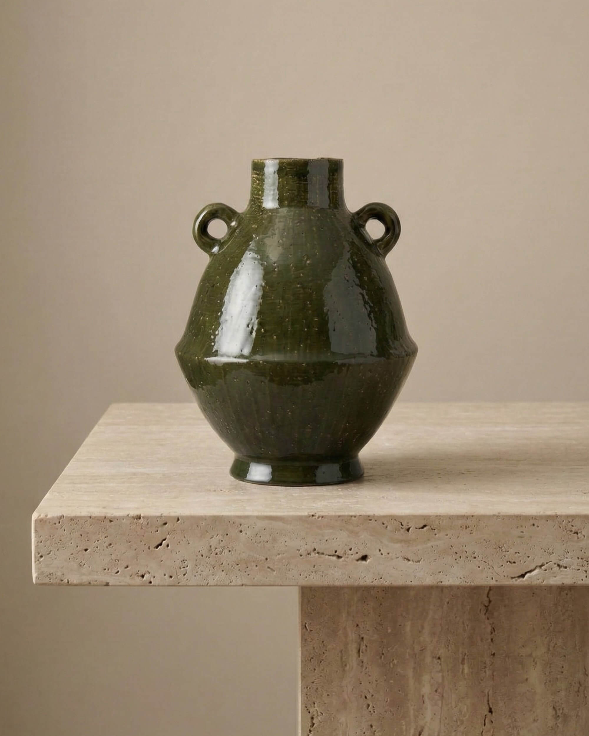 Vase Basile en céramique émaillée vert olive foncé avec deux petites anses. Forme amphore artisanale de 34cm, posé sur une table en travertin. Décoration style méditerranéen et wabi-sabi.